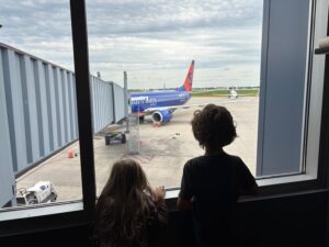 two children looking out a window at an airplane
