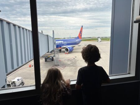 two children looking out a window at an airplane